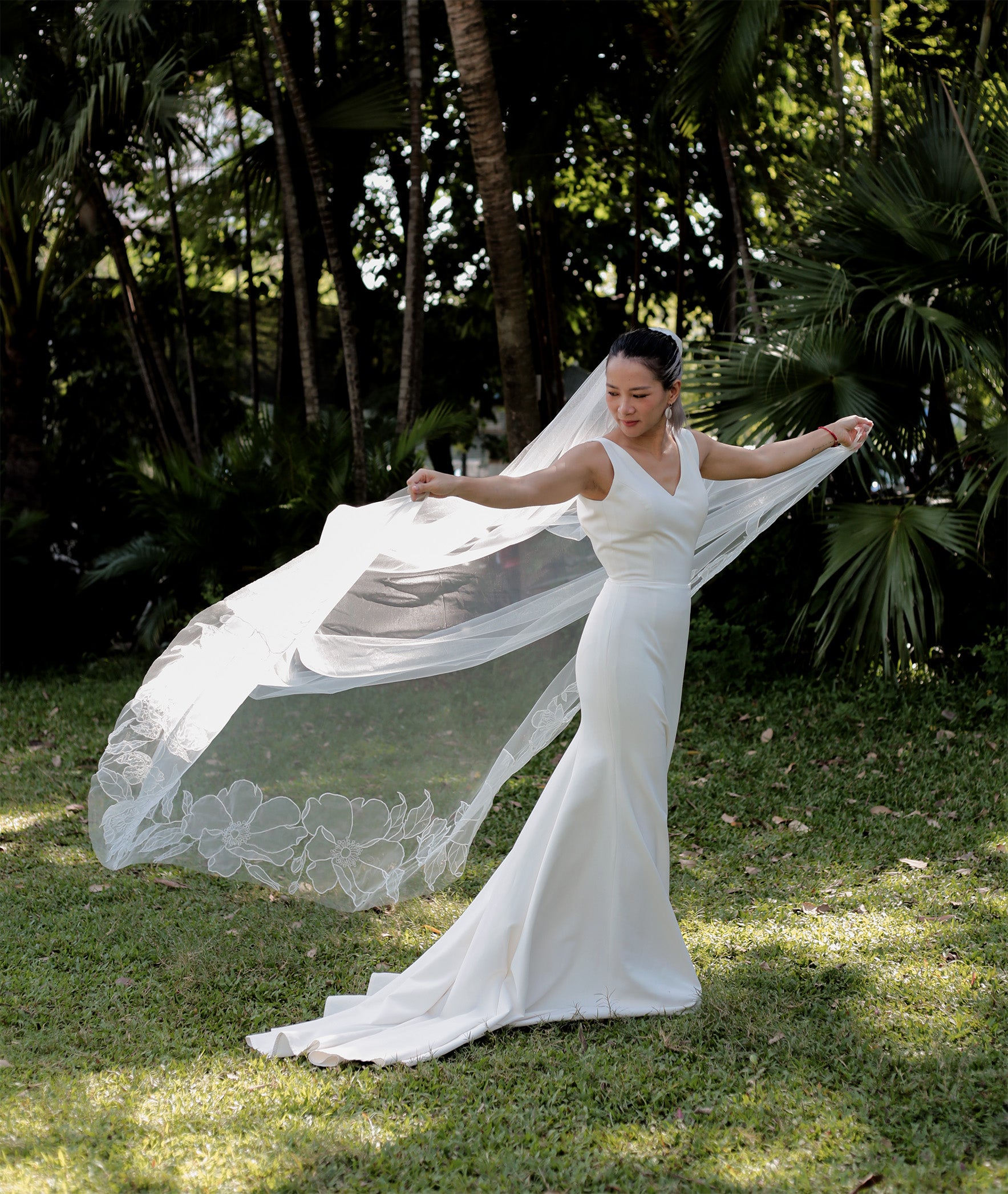 A bride wearing the SOPHIA cathedral veil, showcasing the full length of the flowing organza and the delicate floral pattern from behind.

