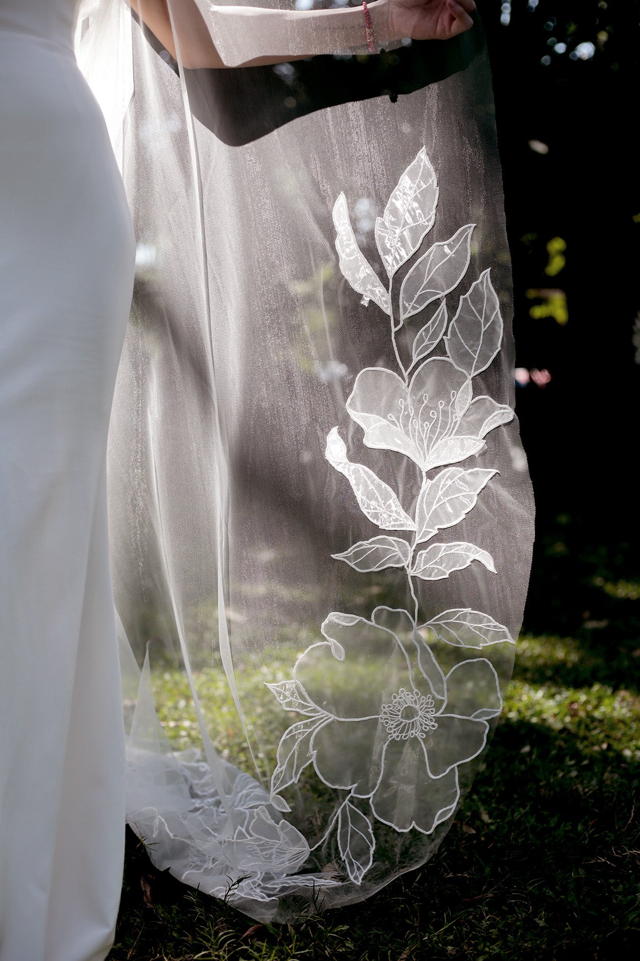 The flowing train of the SOPHIA cathedral organza veil, showcasing the delicate floral lace along the hem.

