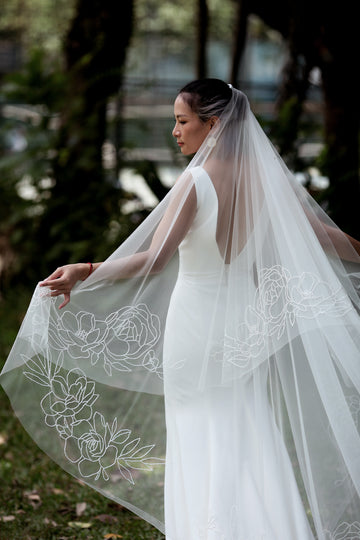 A woman wearing a white cathedral wedding veil with beaded floral embroidery.