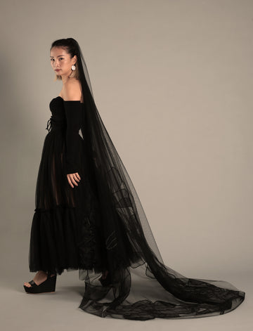 A model wearing a full-length black wedding veil with cosmos flower detailing, paired with a black gown.