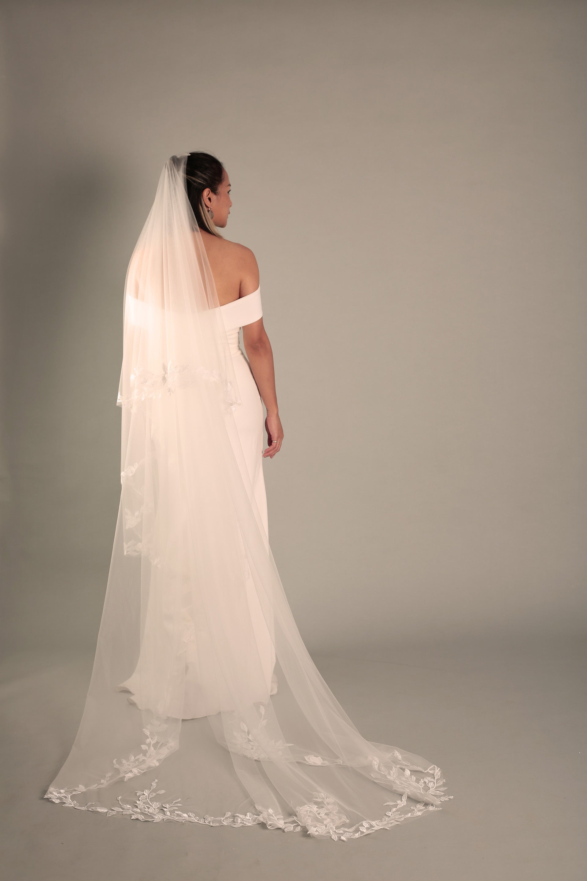 The back view of a bride wearing the BRITTNIE veil, showcasing its full cathedral length and the beautiful floral lace trim.
