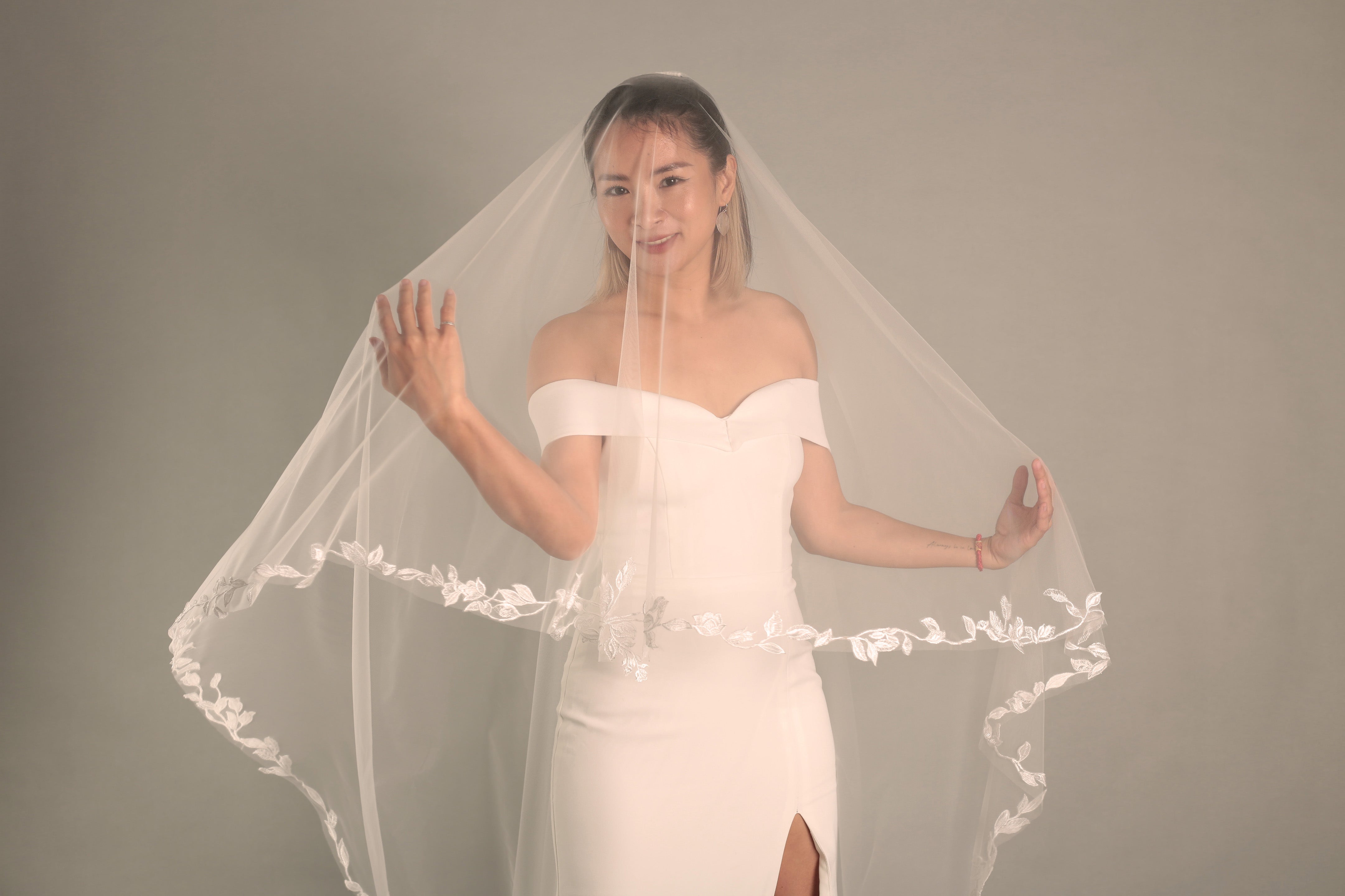 Front view of the BRITTNIE veil, showing the sheer blusher framing the bride's face and the floral lace cascading down.


