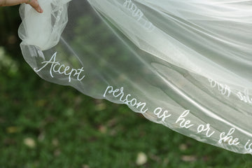 A close-up of a beaded floral wedding veil with embroidered text in a garden setting.