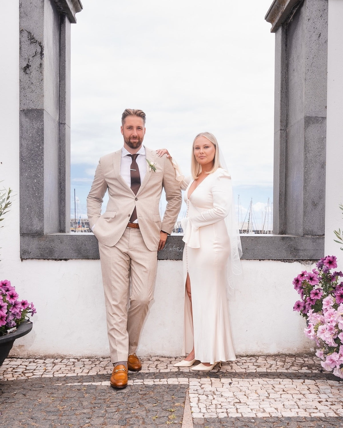 Confident modern bride and groom oceanfront venue in Portugal featuring a fingertip-length floral wedding veil
