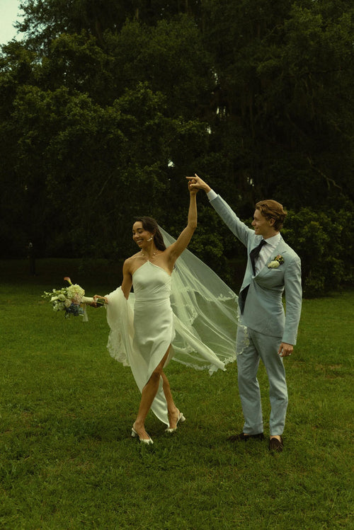 Bride Mckhayla wearing a cathedral-length lace floral veil in a vintage bohemian garden theme wedding kissing under an old giant tree
