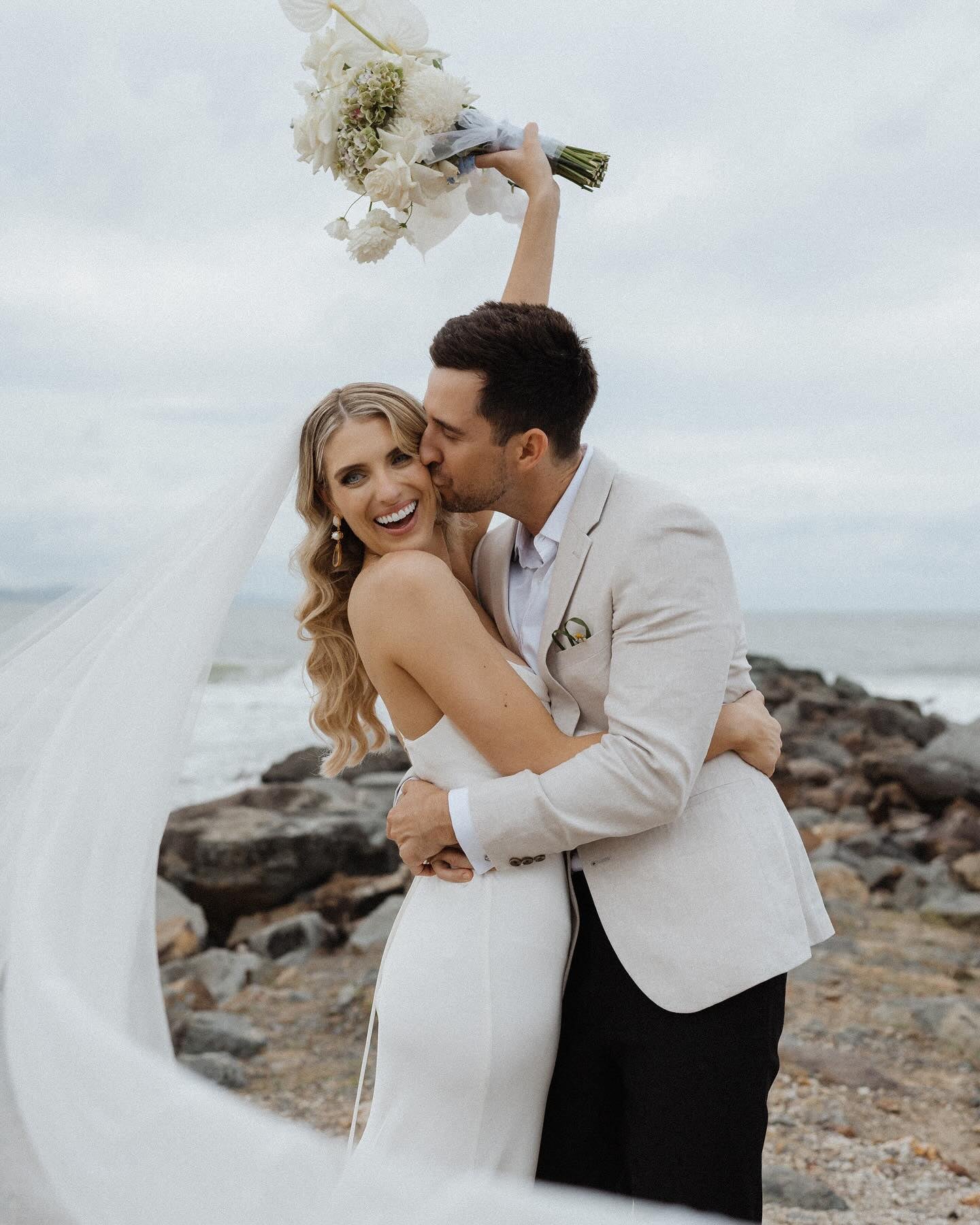 Bride Nicola Fossey with her husband and a floral cathedral veil onseashore