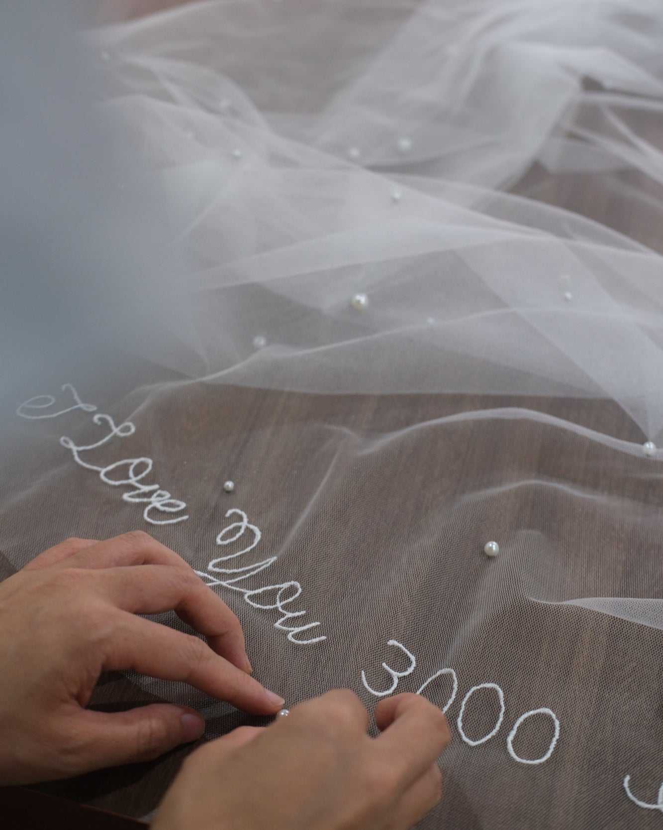 Artisan adding pearl to handmade wedding veil with romantic phrase