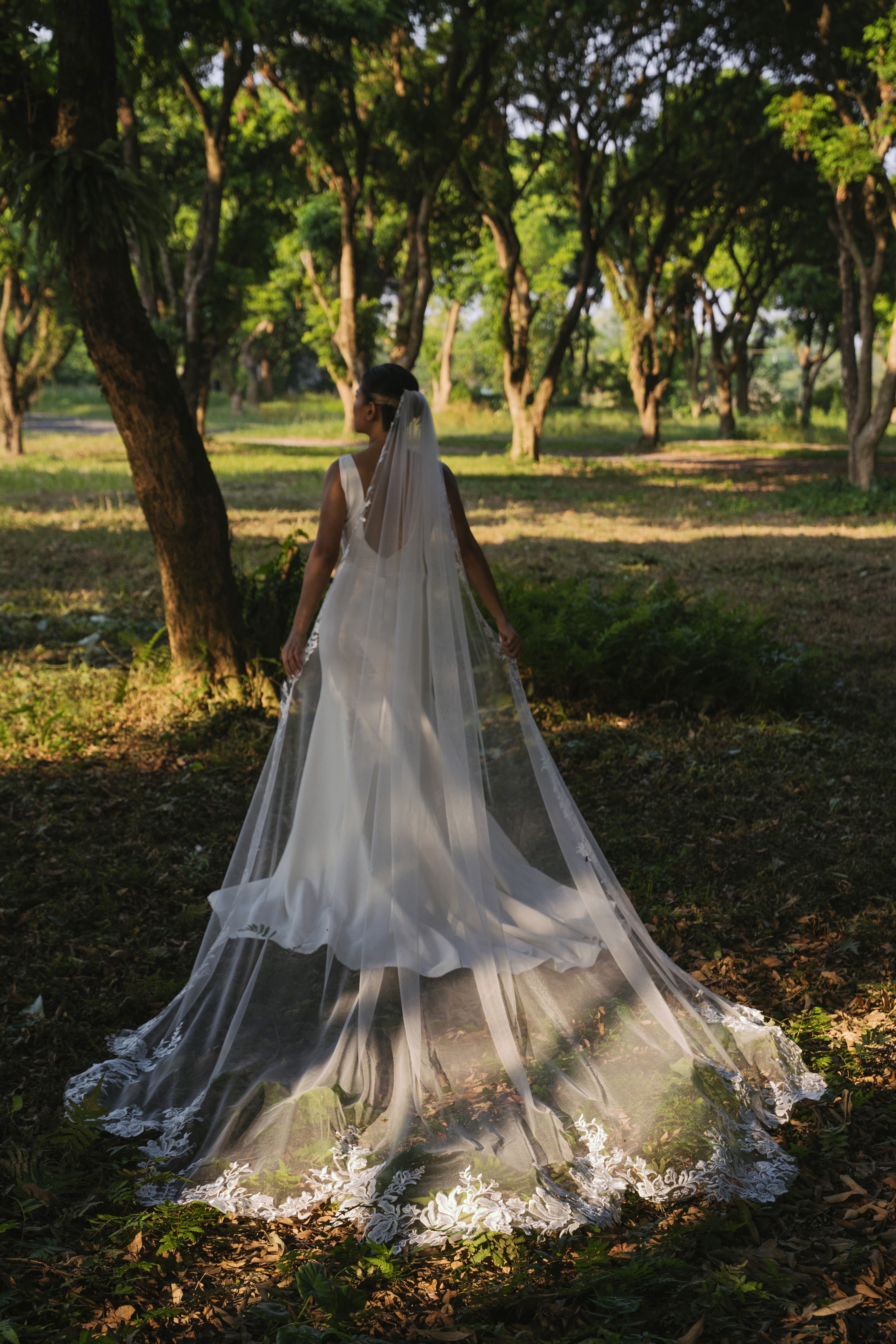 Bride wearing ELA - a lace floral wedding veil walking through a green sunny forest