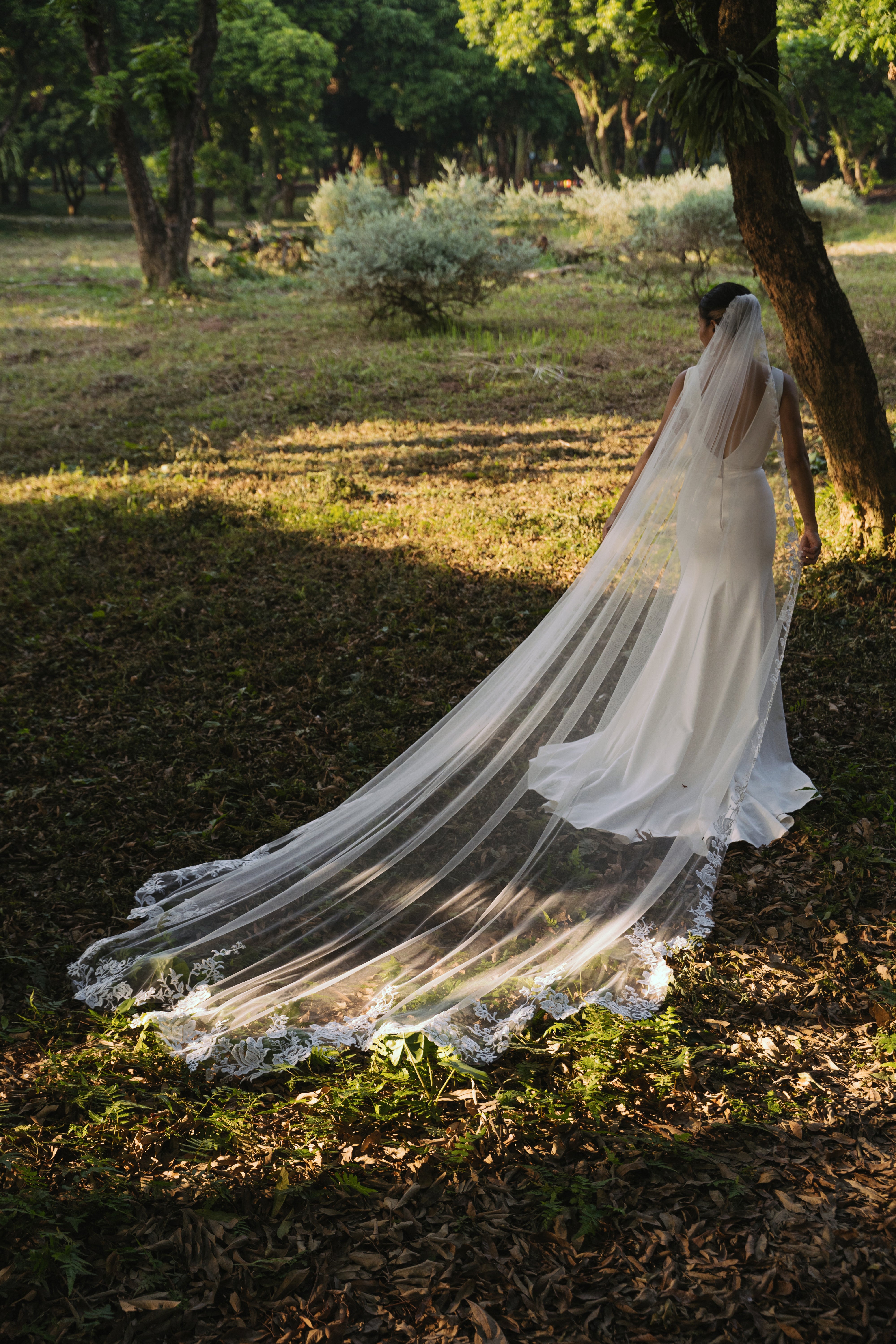 A bride from behind wearing the "ELA" lace veil, highlighting its delicate design.

