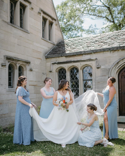 Bride with bridesmaids in a courtyard of a stone building.