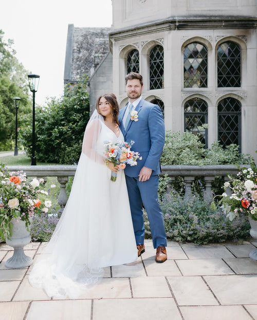 Wedding couple standing in front of a stone building with floral decorations.
