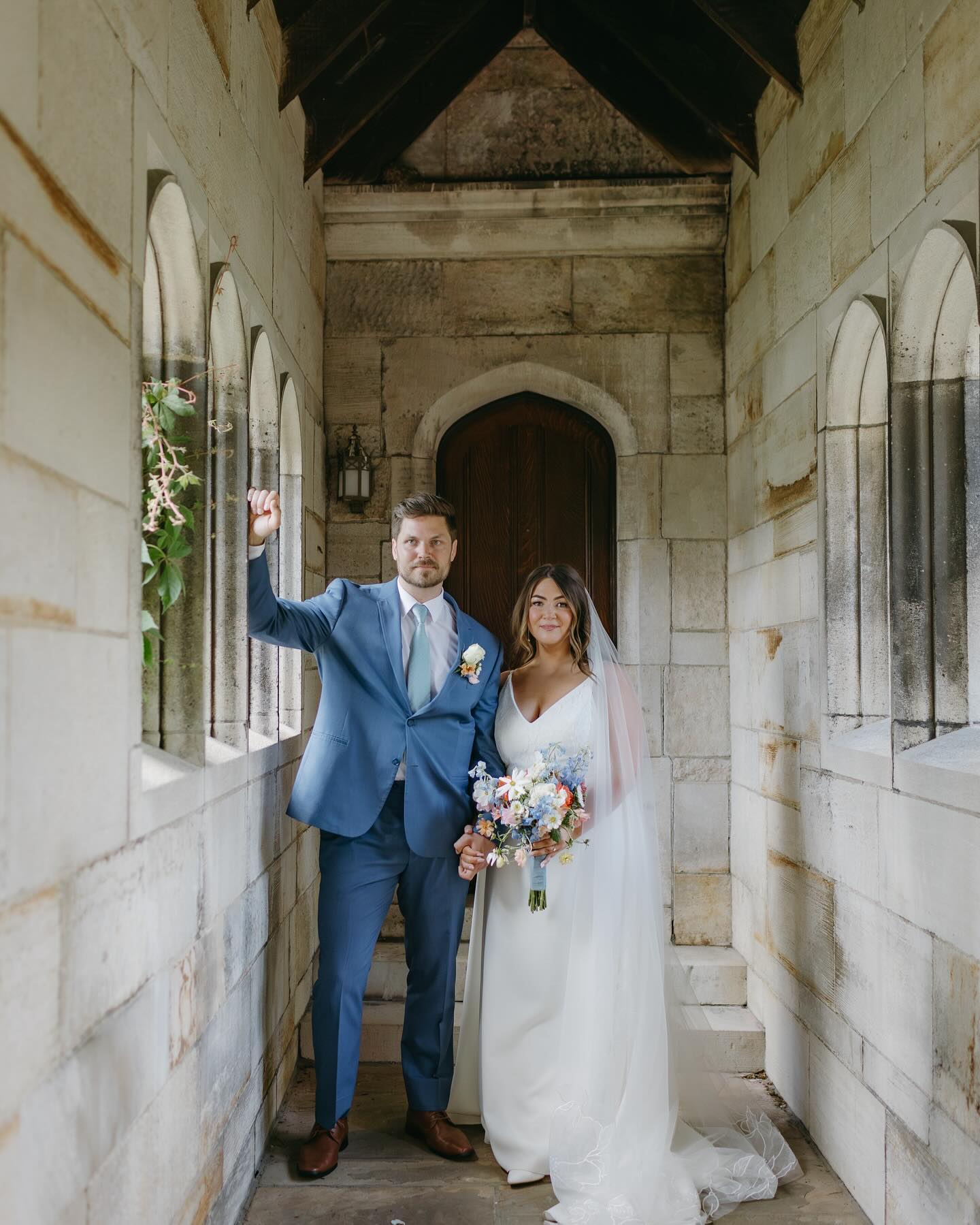 Wedding couple standing in a stone archway.